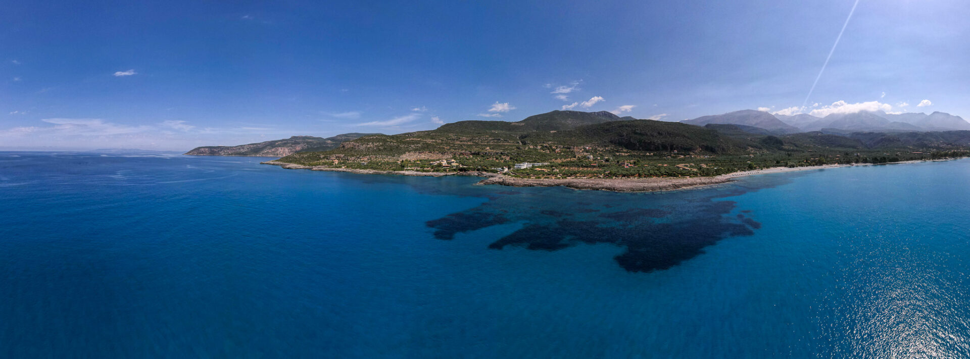 Aerial view of Kardamili’s coastline with clear blue waters, lush greenery, and the Taygetos Mountains in the background